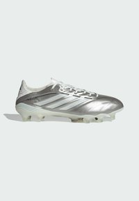 Chaussure de football Adidas Copa argent avec lacets blancs, marquage à trois bandes, et semelle à crampons translucide sur un fond clair uni.
