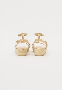 Espadrilles compensées dorées avec une semelle en jute texturée, des brides à la cheville et un dessus en synthétique lisse. Comprend deux boucles et une semelle intérieure rembourrée.