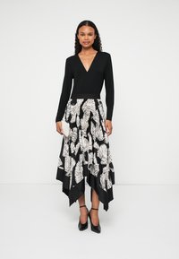 Crno-bijela haljina s uskim gornjim dijelom i lepršavom suknjom s motivima lišća. Dugih rukava, V-izrez, asimetrični rub, uparena s crnim štiklama.