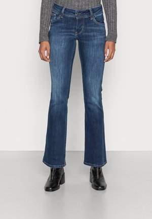 Siniset farkkujen räätälöity malli, jossa on viisi taskua, hienovarainen kuluminen ja kontrastivärinen ompelu, yhdistettynä mustiin nilkkasaappaisiin.