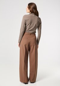 Bruine, gemarmerde blouse met lange mouwen en geometrisch ontwerp, gecombineerd met hoge, brede bruine broeken met achterzakken.