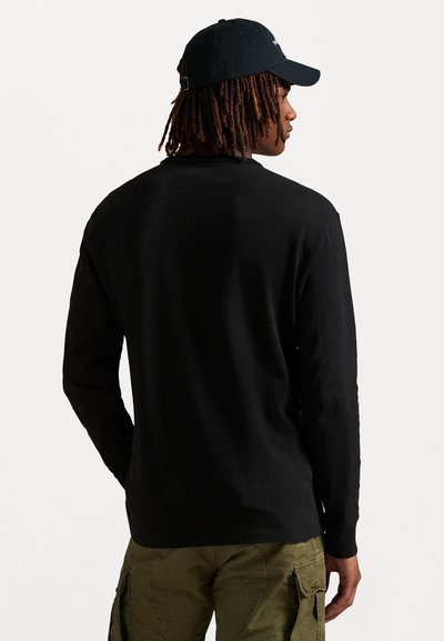 Camisa preta de mangas longas com decote redondo, feita de um tecido macio. Apresenta mangas ajustadas e um design liso nas costas. Combinada com calças cargo em tom oliva.