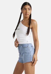 White ribbed one-shoulder tank top with black text, paired with high-waisted light blue denim shorts featuring frayed hem and front pockets.