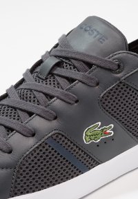 Baskets pour hommes avec dessus en cuir gris et mesh, lacets ronds, logo crocodile vert et semelle en caoutchouc blanche.