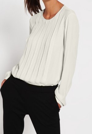 Biała bluzka z długim rękawem, ozdobiona pionowymi plisami i okrągłym dekoltem, zestawiona z czarnymi spodniami dla czystego, neutralnego wyglądu.
