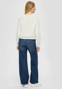 Biały prążkowany sweter dzianinowy o oversize'owym kroju zestawiony z ciemnoniebieskimi dżinsami typu wide-leg o wysokim stanie. Białe trampki na platformie.