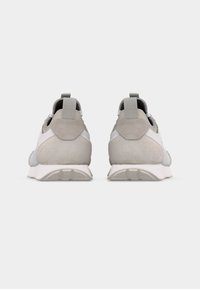 Ζευγάρι ανοιχτόγριων σουέντ και υφασμάτινων αθλητικών παπουτσιών, εμφανιζόμενα από πίσω, με λευκές σόλες και θηλιές για εύκολη εφαρμογή, σε απλό φόντο.