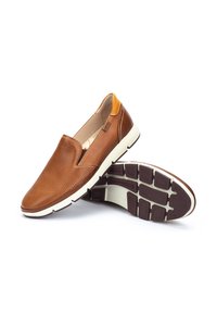 Zapato marrón de piel sin cordones con diseño perforado, detalle amarillo en el talón y suela de goma blanca con patrón de relieve.