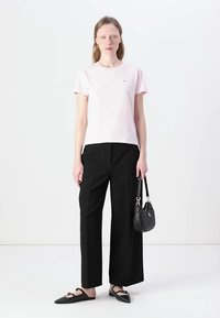 Tricou din bumbac roz deschis, pantaloni negri drepti, pantofi negri cu talpă joasă și o poșetă mică neagră. Ținută simplă, casual.