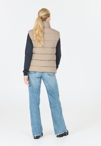 Beige pufferväst med hög krage, med horisontella quiltade sektioner. Buren över en svart långärmad tröja och i kombination med ljusblå jeans.