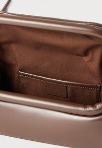 Καφέ ορθογώνια τσάντα με δερμάτινο πλαίσιο, υφασμάτινη εσωτερική επένδυση και ραμμένη τσέπη με δερμάτινη επένδυση ραμμένη και μικρή ετικέτα.