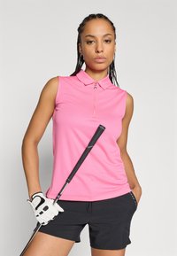 Rožinė be rankovių polo marškinėliai su užtrauktuku prie apykaklės ir tekstūruota medžiaga, derinami su juodomis šortais ir golfu klube, laikomame rankoje, taip pat baltos pirštinės.