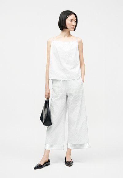 Γυναίκα που φορά λευκό αμάνικο τοπ και φαρδιά παντελόνια cropped με λεπτές ρίγες, κρατώντας μαύρη τσάντα χειρός και φορούν μαύρες μπαλαρίνες.