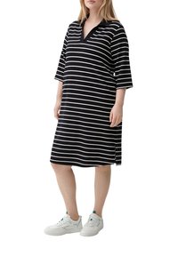 Abito a righe bianche e nere con colletto in stile polo, maniche a tre quarti, spacchi laterali, abbinato a scarpe da ginnastica bianche. Tessuto dalla texture morbida.