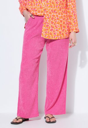 Lyserøde bukser med vide ben kombineret med en orange og lyserød leopardprint langærmet skjorte og sorte flip-flops.