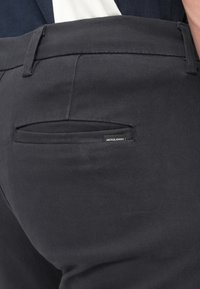 Pantalon gris foncé en tissu texturé, avec une petite poche arrière et une étiquette noire affichant "JACK & JONES". Design simple et droit.