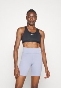 Black sports bra with a Nike logo, paired with lavender high-waisted shorts, showcasing a smooth texture and fitted design.