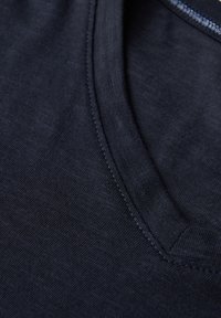 Maglietta navy a V realizzata in tessuto testurizzato, con un colletto pulito e una discreta finitura cucita, che enfatizza un design semplice e casual.