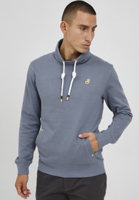 Felpa grigia con colletto alto, con lacci bianchi e logo giallo. Presenta tasche laterali con dettagli gialli e polsini a coste.
