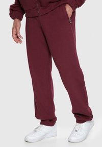 Bordeaux joggerbukser lavet af blødt stof, med sidelommer og en fitted manchet-design. Sorte med hvide sneakers for kontrast.