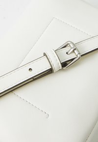 La tracolla della borsa in pelle bianca presenta una fibbia in metallo silver, con cuciture pulite e un design geometrico sulla superficie della borsa.