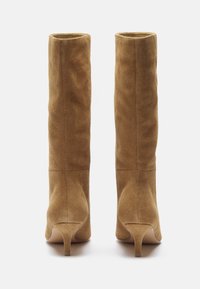 Alti stivali in suede marrone con tacco affusolato. Texture liscia, dettagli di cucitura minimi e design a cima aperta.