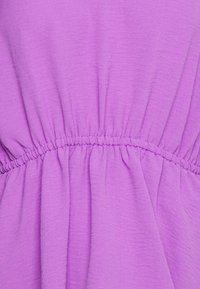 Tessuto viola con una finitura testurizzata, dotato di una cintura elastica che crea un effetto arricciato per un maggiore volume e fluidità.