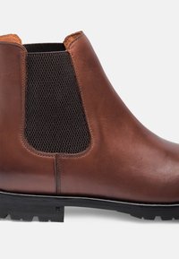 Stivale Chelsea in pelle marrone con pannelli laterali elasticizzati, mesh nera testurizzata e una robusta suola in gomma con un leggero motivo di battistrada.