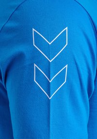 Blauwe kortekorte mouwen shirt met een gestructureerde stof. Witte grafiek van twee naar beneden wijzende chevrons die verticaal op de achterkant zijn uitgelijnd.