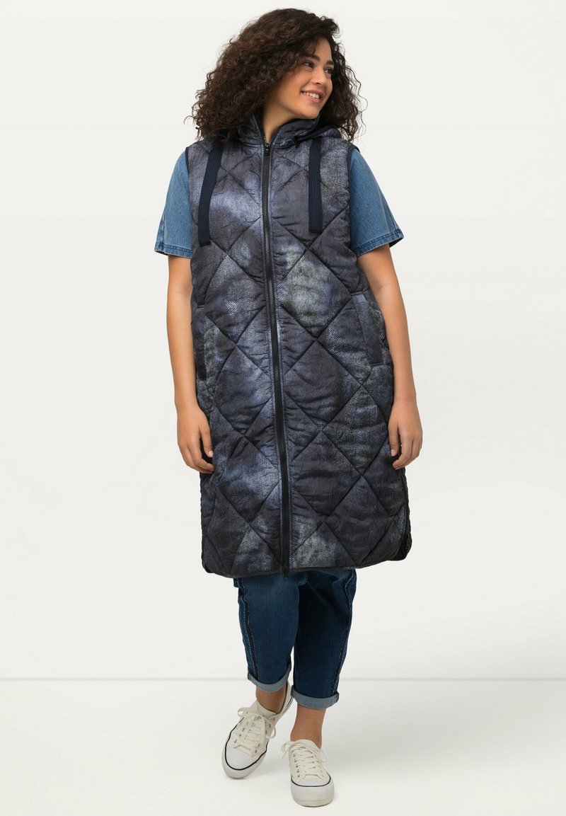Gep puffter ärmelloser marineblauer Weste mit strukturiertem Muster, Frontreißverschluss und Kordelzugkapuze. Tragen über einem Jeanshemd und gestylt mit Jeans.
