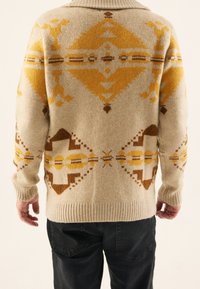 Stickad tröja i krämfärgad med geometriska mönster i gult, brunt och beige. Har en ribbad krage och manschetter, medellång längd och avslappnad passform.