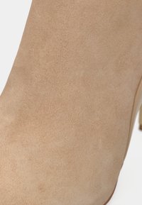 Gheata bej din piele întoarsă, cu o textură netedă, formă elegantă și vârf ascuțit. Are un toc subțire și detaliu subtil de cusătură.