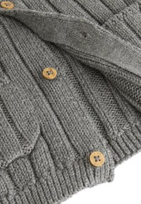 Cardigan gris tricoté avec côtes texturées, boutons en bois et motif en torsades. Matière douce en laine avec des points apparents.