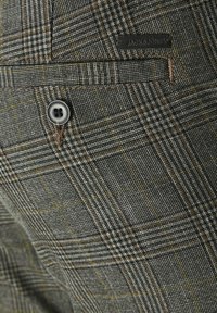 Tissu à carreaux gris présentant un motif distinct avec des fines lignes dans des tons marron foncé et des accents jaunes. Comprend un bouton et un patch logo.
