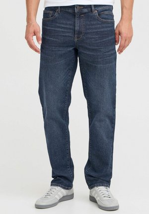 Mørkeblå denimjeans med en klassisk rett passform, subtil falming og sydd detaljer. Brukt med grå sportssko.