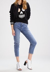 Svart bomberjacka med vita ränder, t-shirt med dödskallegrafik, ljusblå cropped jeans, vita klackboots med dragkedjedetalj.