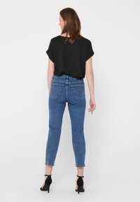Svart kortermet topp og blå høytlivsjeans med klassisk femlommestil, tettsittende snitt og ankellang hem. Svart hæl sandaler.
