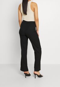 Černé kalhoty na míru se střihovým designem rovného nohavice, doplněné béžovým bezrukávovým topem. Hladká látka a minimalistické detaily.