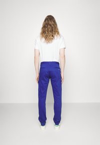 Modré cargo kalhoty se dvěma bočními kapsami, prošitými švy a rovný střih, spárované s bílým tričkem a světlými teniskami.