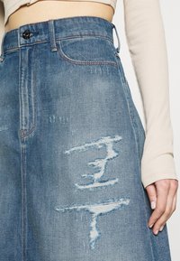 Denim A-linjekjol i ljusblått, med slitna lappar och fransade kanter. Inkluderar klassisk midja med knapp och bältesöglor.