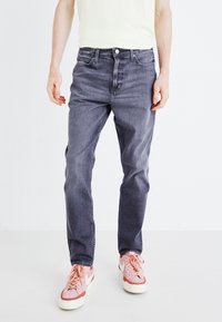 Moške sive denim hlače s ravnim krojem, opremljene s petimi žepi, gumbom za zapiranje in rahlo zbledelim materialom. V kombinaciji z roza športnimi copati.