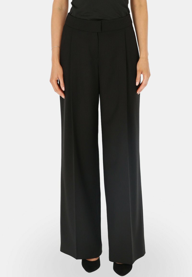 Czarne spodnie o szerokich nogawkach z gładką teksturą, z plisowanym przodem i dopasowaną talią. Noszone z prostą bluzką i czarnymi butami.
