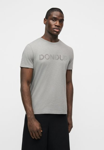 Νέος Μαύρος άνδρας που φοράει ανοιχτό γκρι κοντομάνικη φανέλα με το λογότυπο "DONDUP" και μαύρο σορτς, στέκεται μπροστά σε απλό λευκό φόντο.