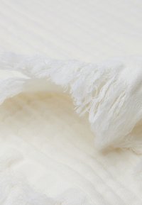 Witte textuurstof met franjes aan de randen, voorzien van een subtiel patroon. Zacht en lichtgewicht, geschikt voor diverse toepassingen.