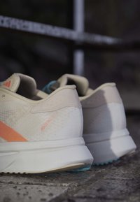Pair of beige Adidas Adizero SL 2 running shoes with light orange details resting on a textured stone surface.