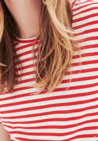 Rood-wit gestreepte t-shirt met een ronde halslijn, gemaakt van zachte stof. Zichtbaar haar bedekt gedeeltelijk de schouder van het shirt.