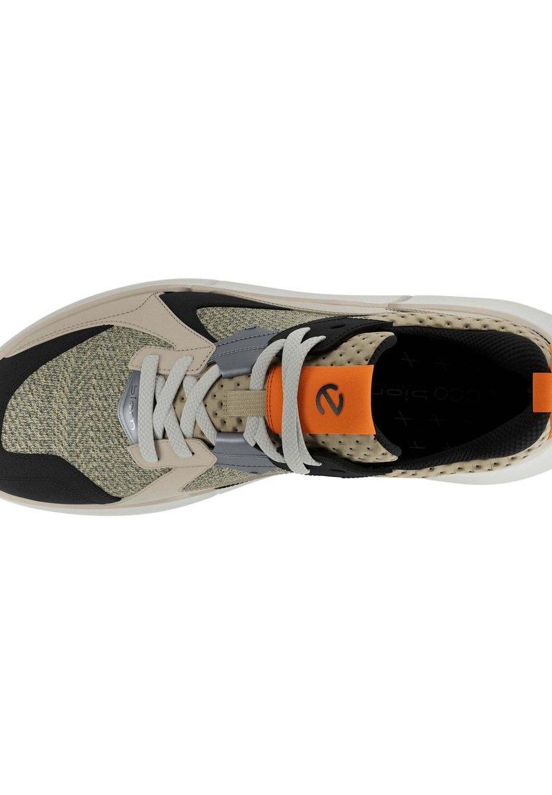 Sneaker mit einem gewebten beigen Obermaterial, schwarzem Gummikap, grauen Akzenten, weißen Schnürsenkeln und einer orangen Fersenschlaufe. Texturiertes Oberflächendesign sichtbar.
