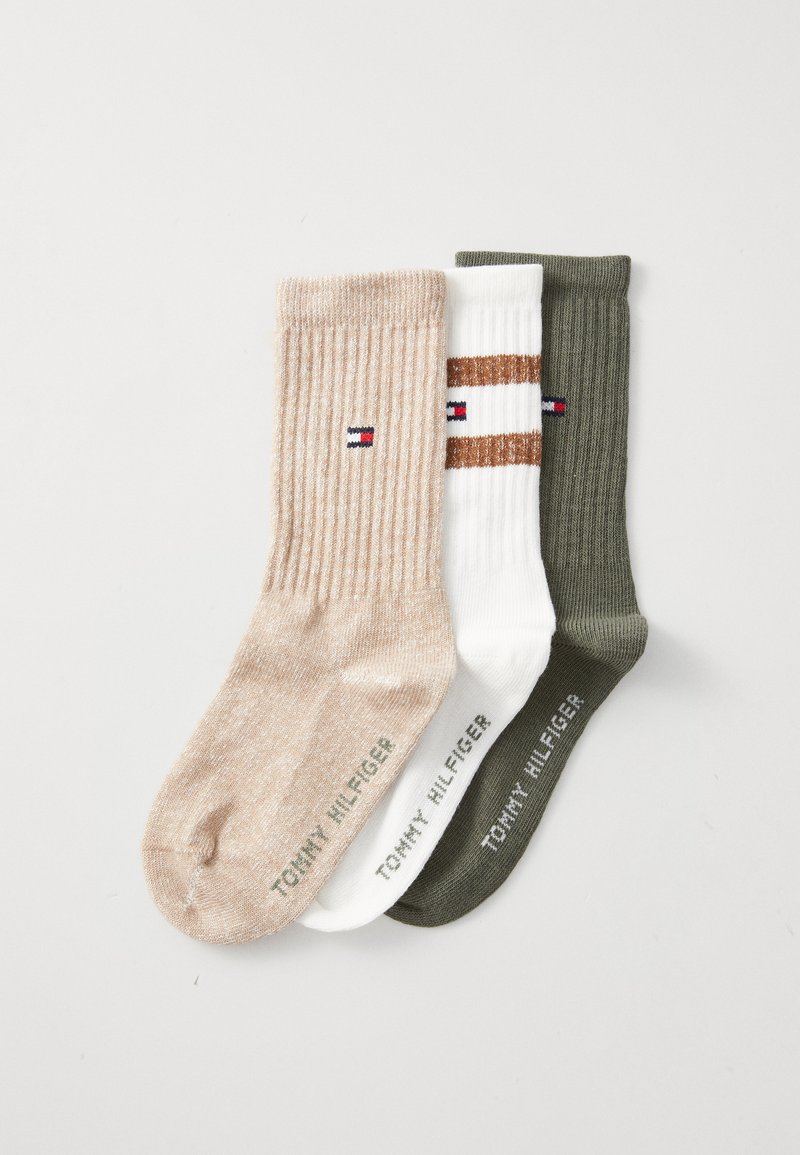 Tre par med ribbestrikkede sokker: lys beige, hvit med brune striper, og mørkegrønn. Hver av dem har en logo på ankelen og strukturert stoff.