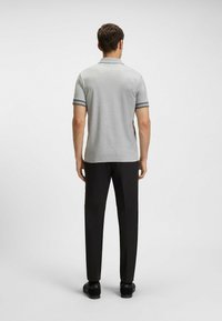 Polo grigio con strisce scure sulle maniche, abbinato a pantaloni neri. Il tessuto appare liscio e la vestibilità è standard.