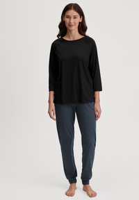 Zwart top met driekwart mouwen en een ronde hals, gecombineerd met lichtblauwe pyjamabroek met stippen en taps toelopende boorden. Soepele, casual stof.